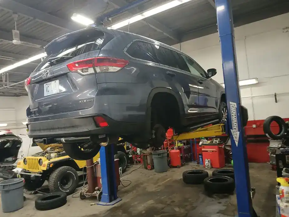 An SUV raised on a two-post lift with tires racked along the wall of the Ray's Travelers bay