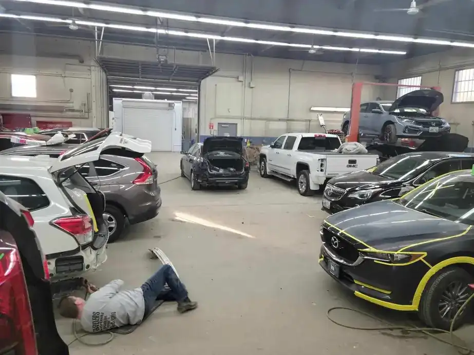 A busy shop floor with several cars mid-repair and panels masked in yellow tape