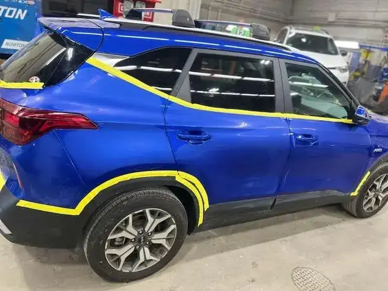 A blue SUV masked in yellow tape and ready for paint