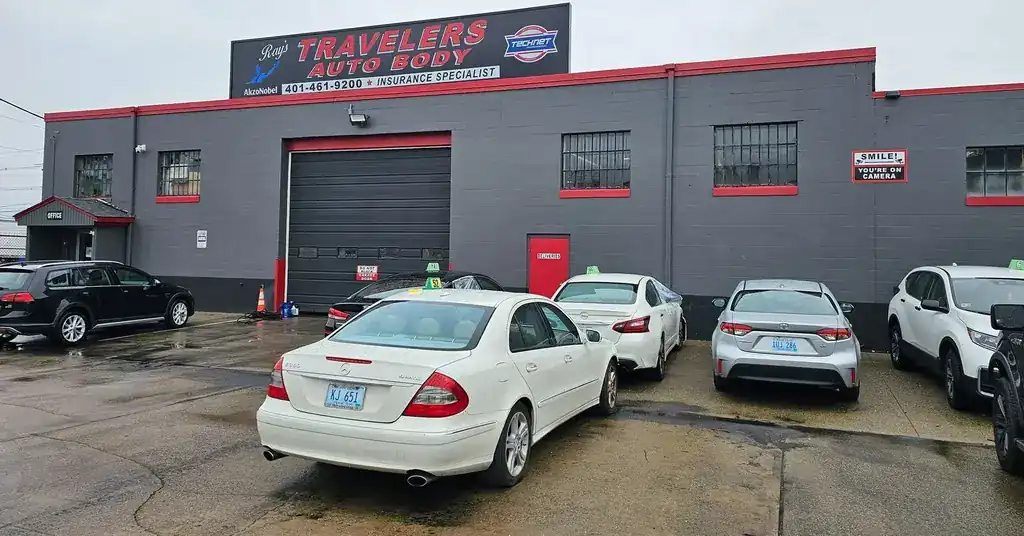 The charcoal block building at 299 Allens Ave with red trim round the windows and bay door, and the Ray's Travelers sign on the roof