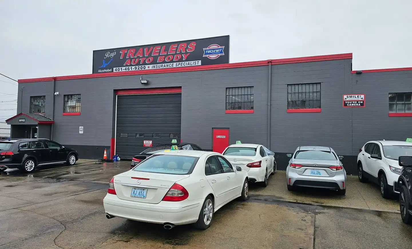 The charcoal block building at 299 Allens Ave with red trim round the windows and bay door, the sign above, and cars in the lot