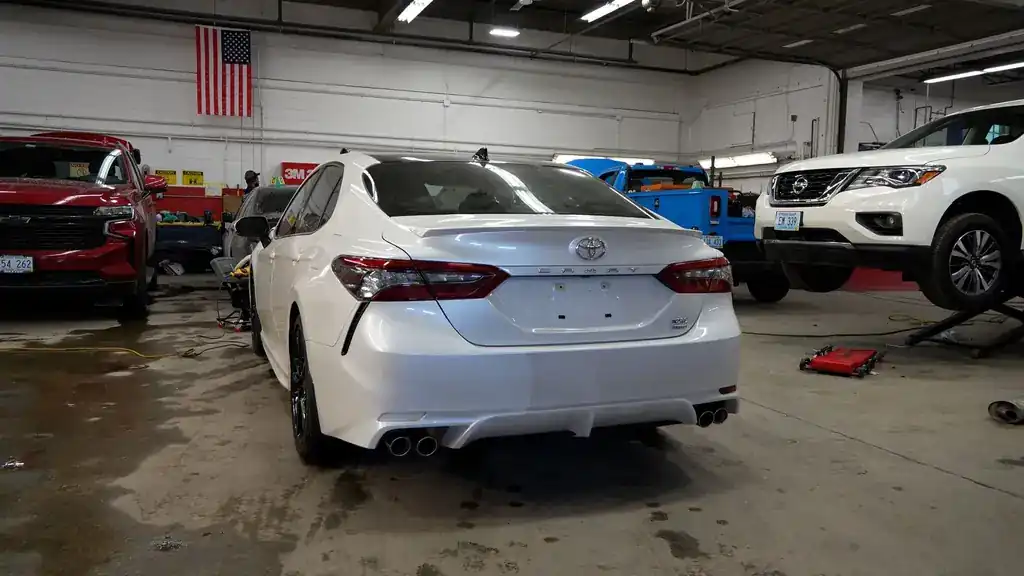 Inside the collision bay: a white Camry, an SUV on the lift and the flag on the back wall