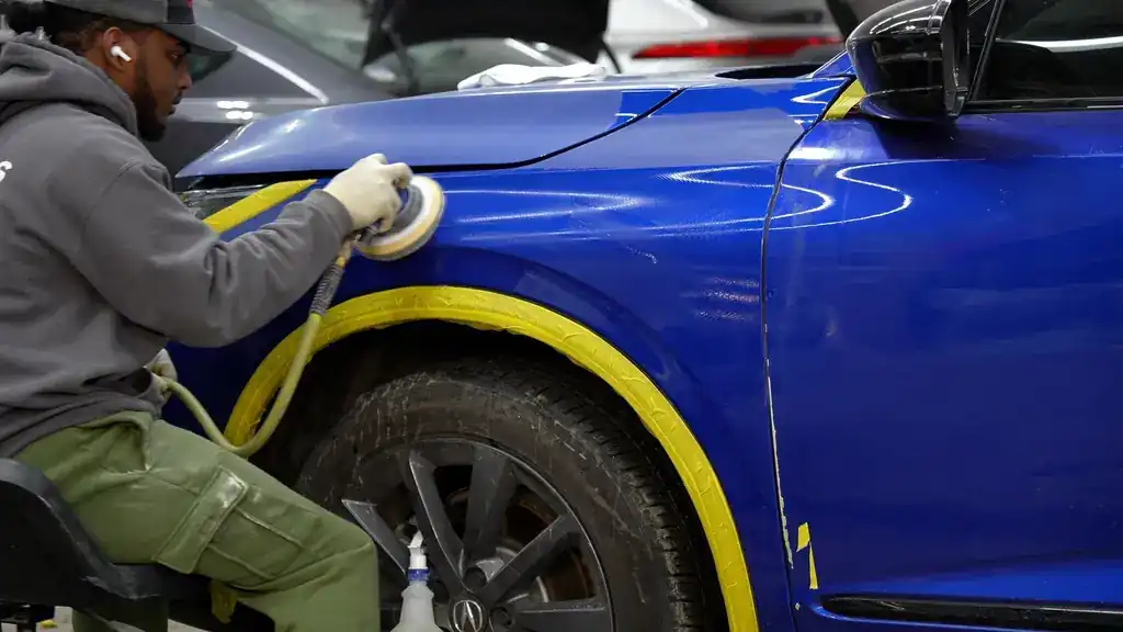 A technician polishing a blue panel with masking tape still along the edge