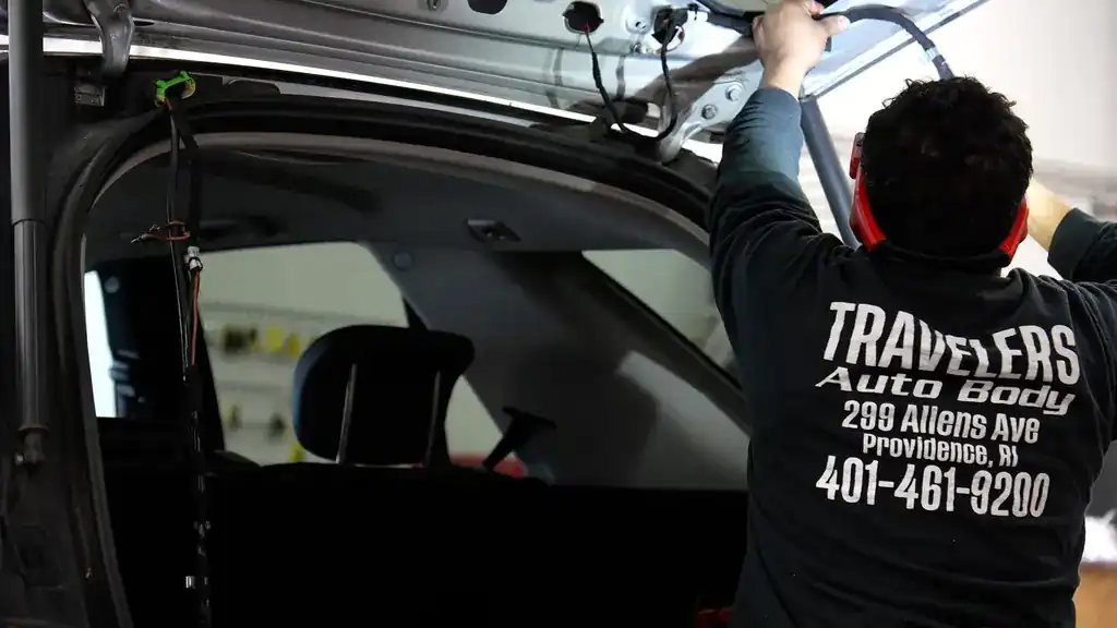 A technician working inside a door in a jacket lettered Travelers Auto Body, 299 Allens Ave