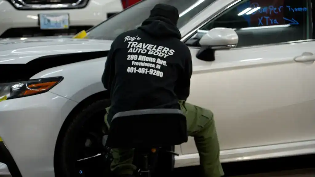 A technician at a white Toyota with the back of the shop jacket toward the camera